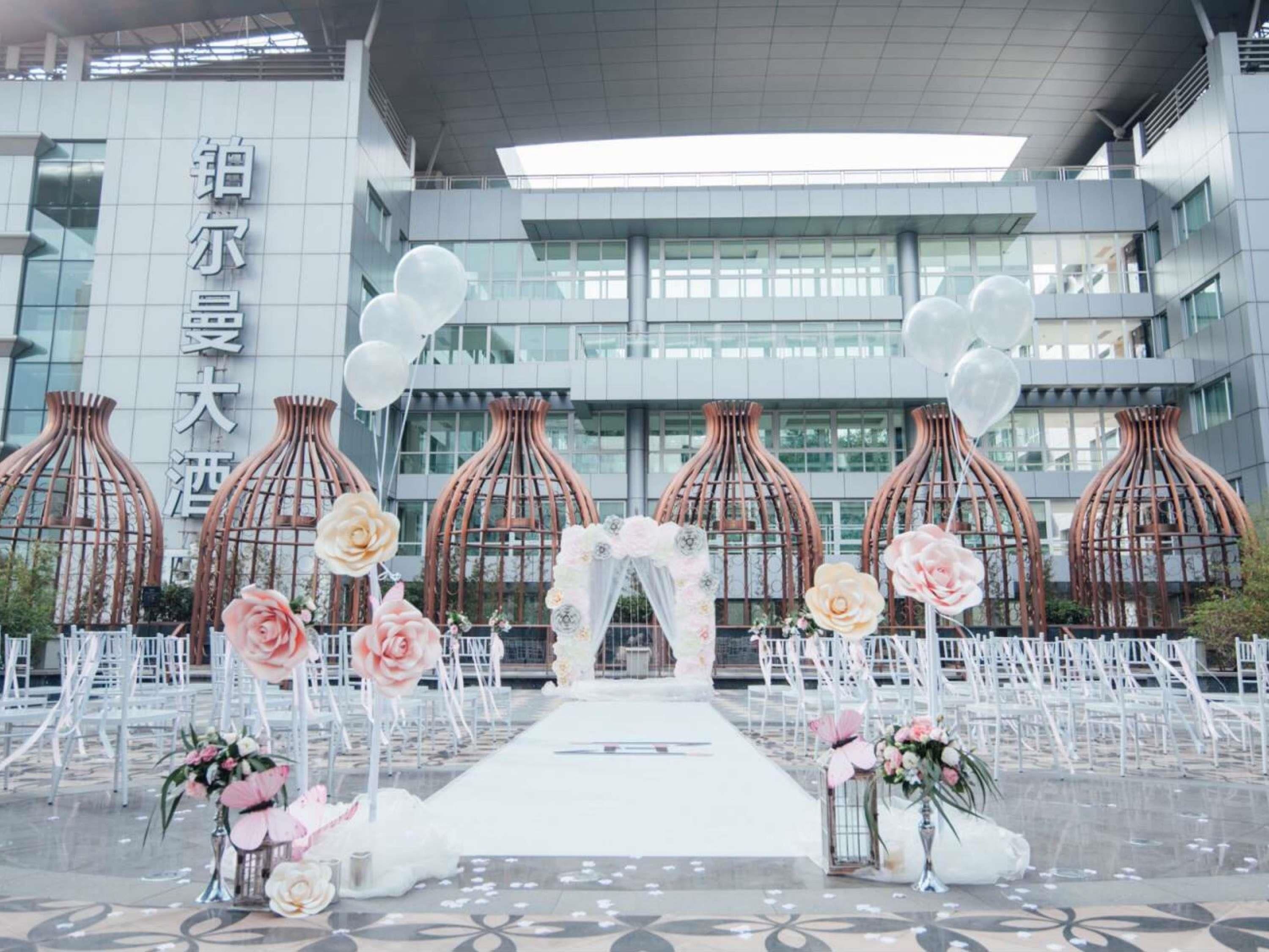 Preparación para una ceremonia de boda con un pasillo blanco, decoración floral y un edificio moderno al fondo.