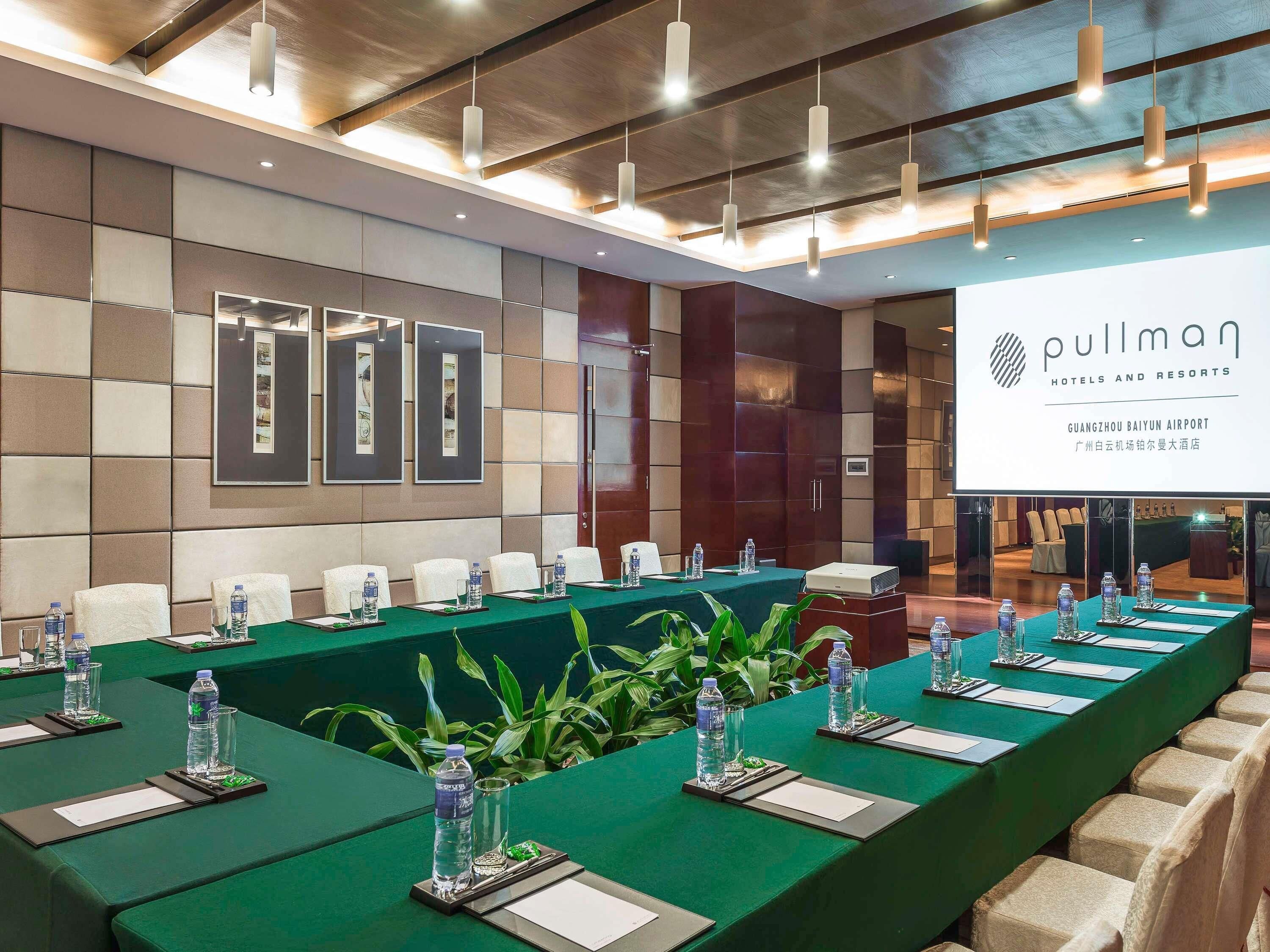 A conference room with a long table, chairs, water bottles, glasses, and a projector.