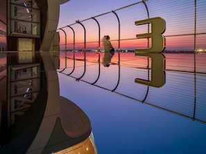 Un edificio moderno con un gran letrero del número 3, barandilla de cristal y vista del atardecer sobre el agua.