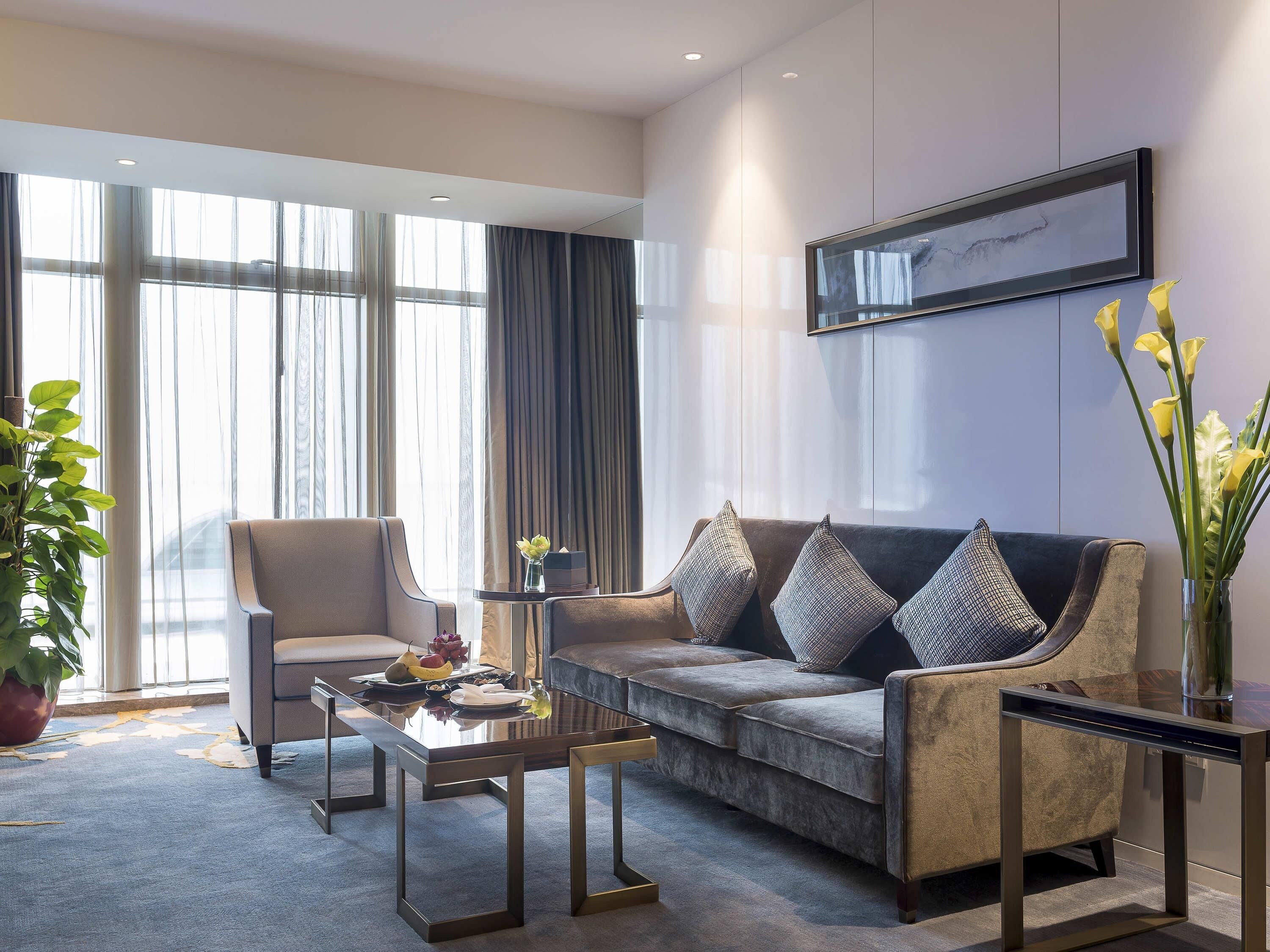 A modern living room with a sofa, armchairs, a coffee table, and a large window with curtains.