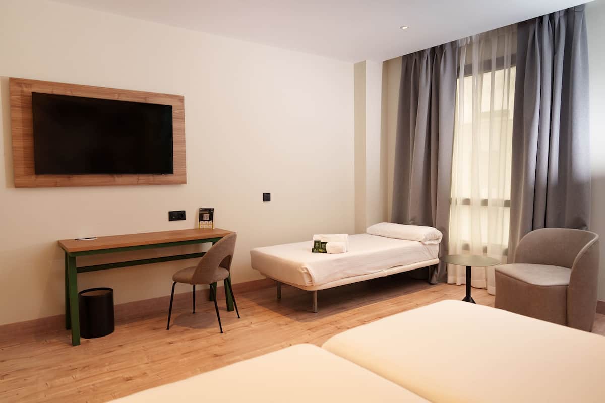 Habitación de hotel con un escritorio de madera, una cama, una silla y un televisor montado en la pared.