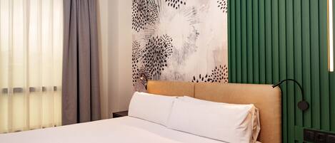 Une chambre d’hôtel avec un lit, une tête de lit, une table de chevet, une télécommande et un mur orné d’un panneau vert et d’un grand tableau abstrait.