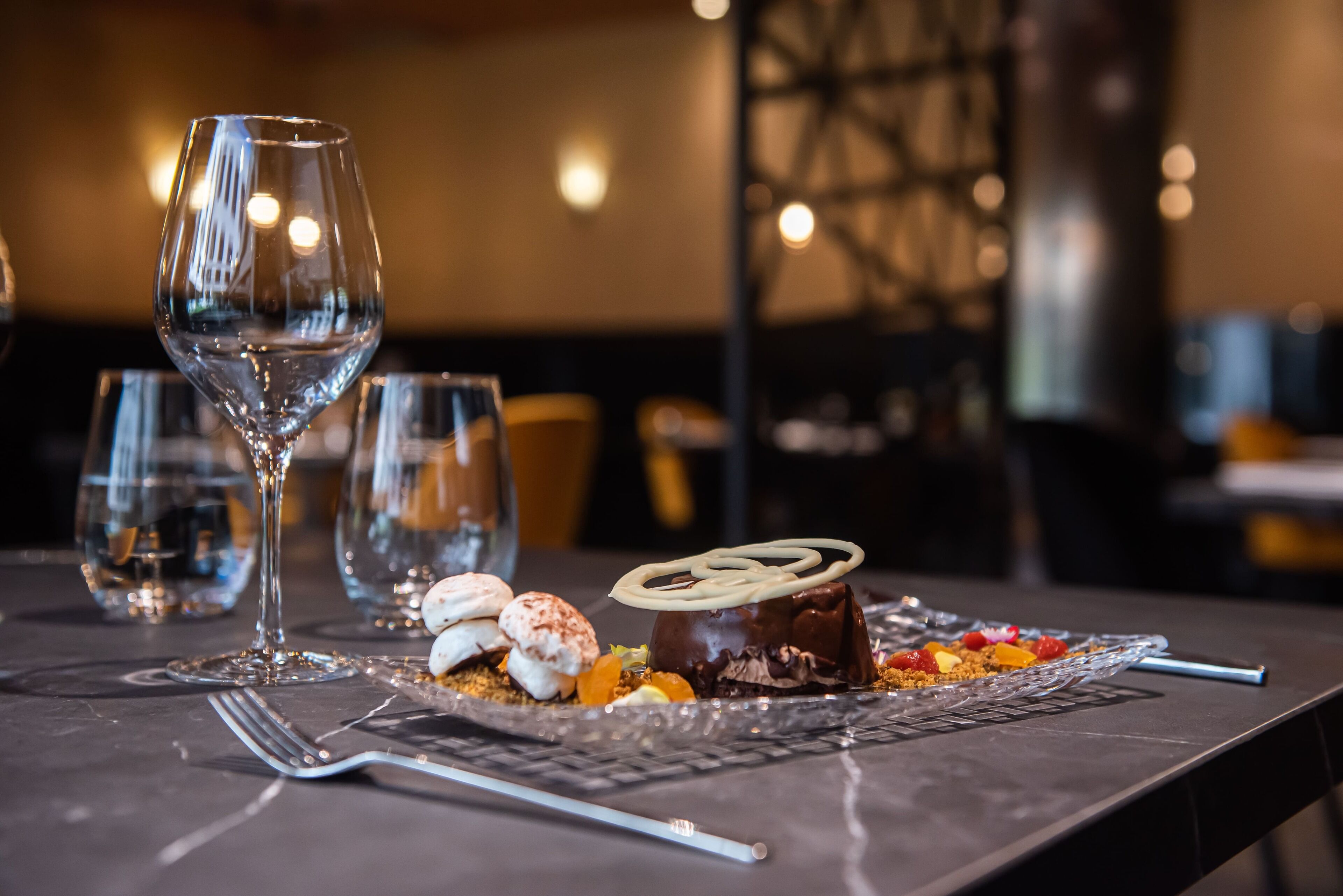 Un piatto da dessert con torta al cioccolato e marshmallow su un tavolo con bicchieri da vino.