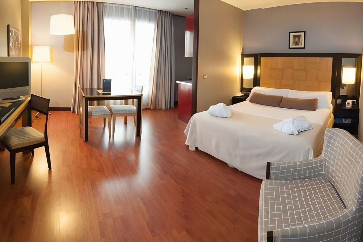 Ein Hotelzimmer mit einem Bett, einem Schreibtisch mit Stuhl, einem Fernseher und einem Badezimmer.