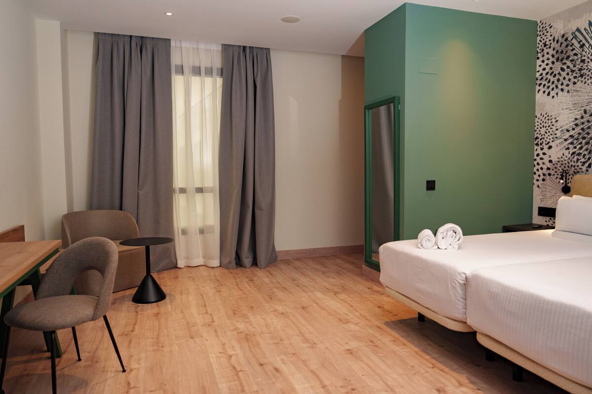 Una habitación de hotel con cama, una silla, una mesita y una puerta.