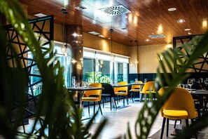 Interior de restaurante con techo de madera, sillas amarillas y ventanas amplias.