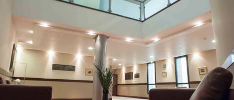 A spacious lobby with a high ceiling, a glass railing, and a central column with a plant.