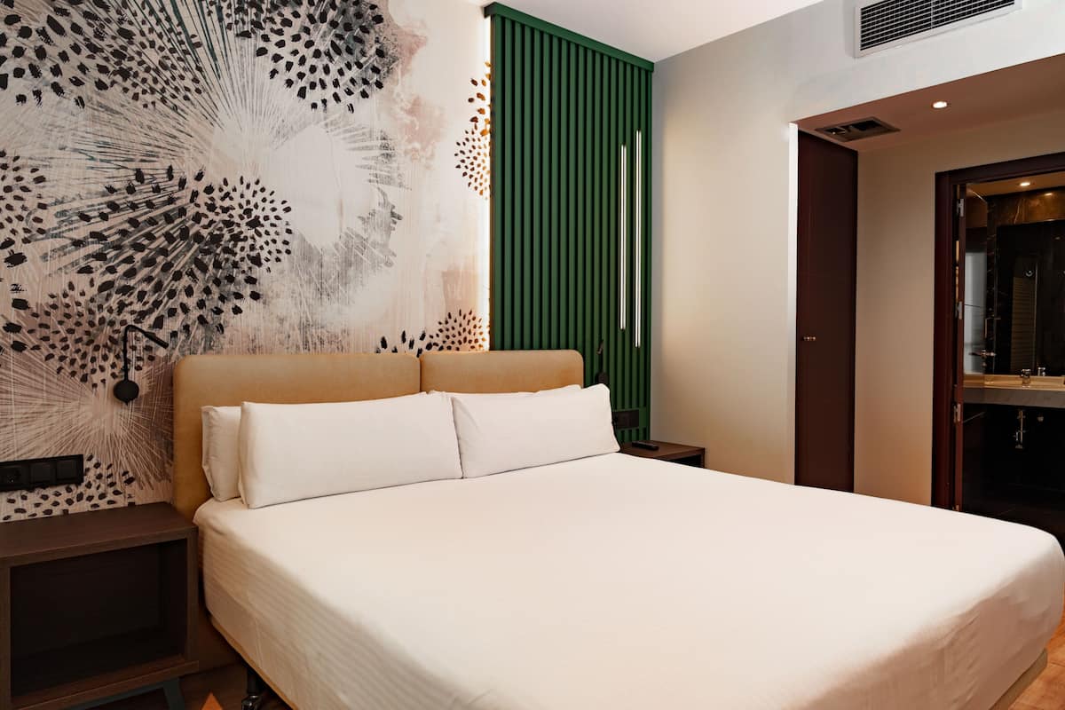 Una habitación de hotel moderna con una cama grande, una pared de acento verde y una pieza de arte decorativa.