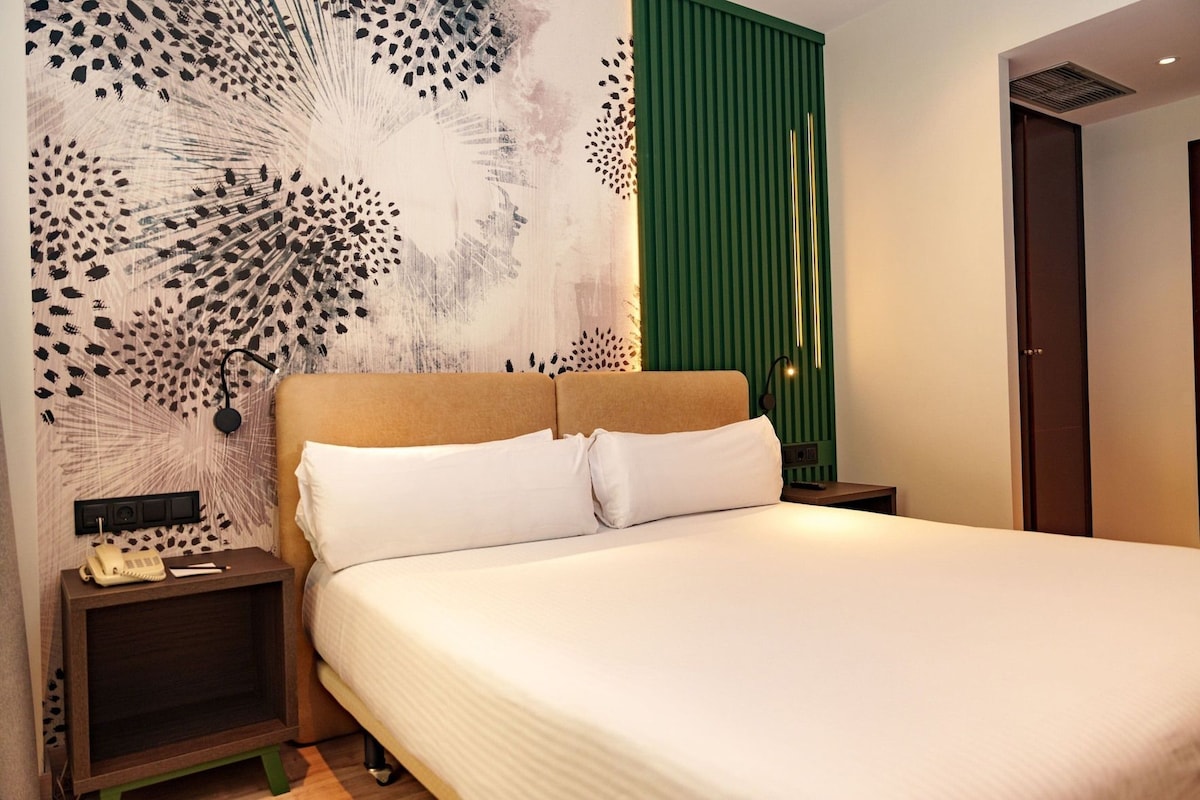 Ein Hotelzimmer mit einem großen Bett, einem Nachttisch mit Telefon und einer Wand mit einem einzigartigen, abstrakten Muster.