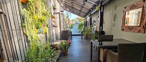 A covered walkway with potted plants, wicker furniture, and a metal railing.