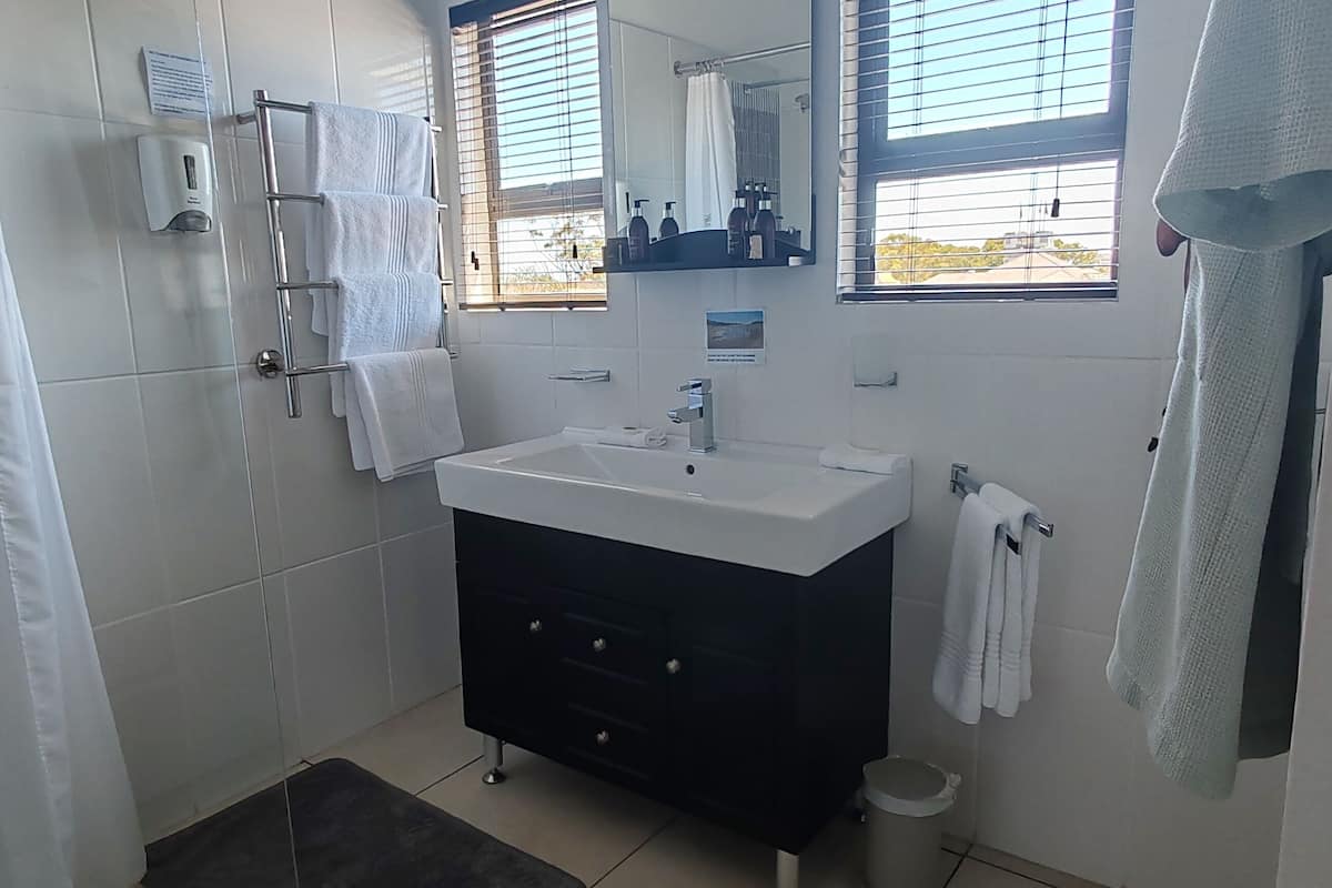 A modern bathroom with a white sink, dark vanity, and a shower area.