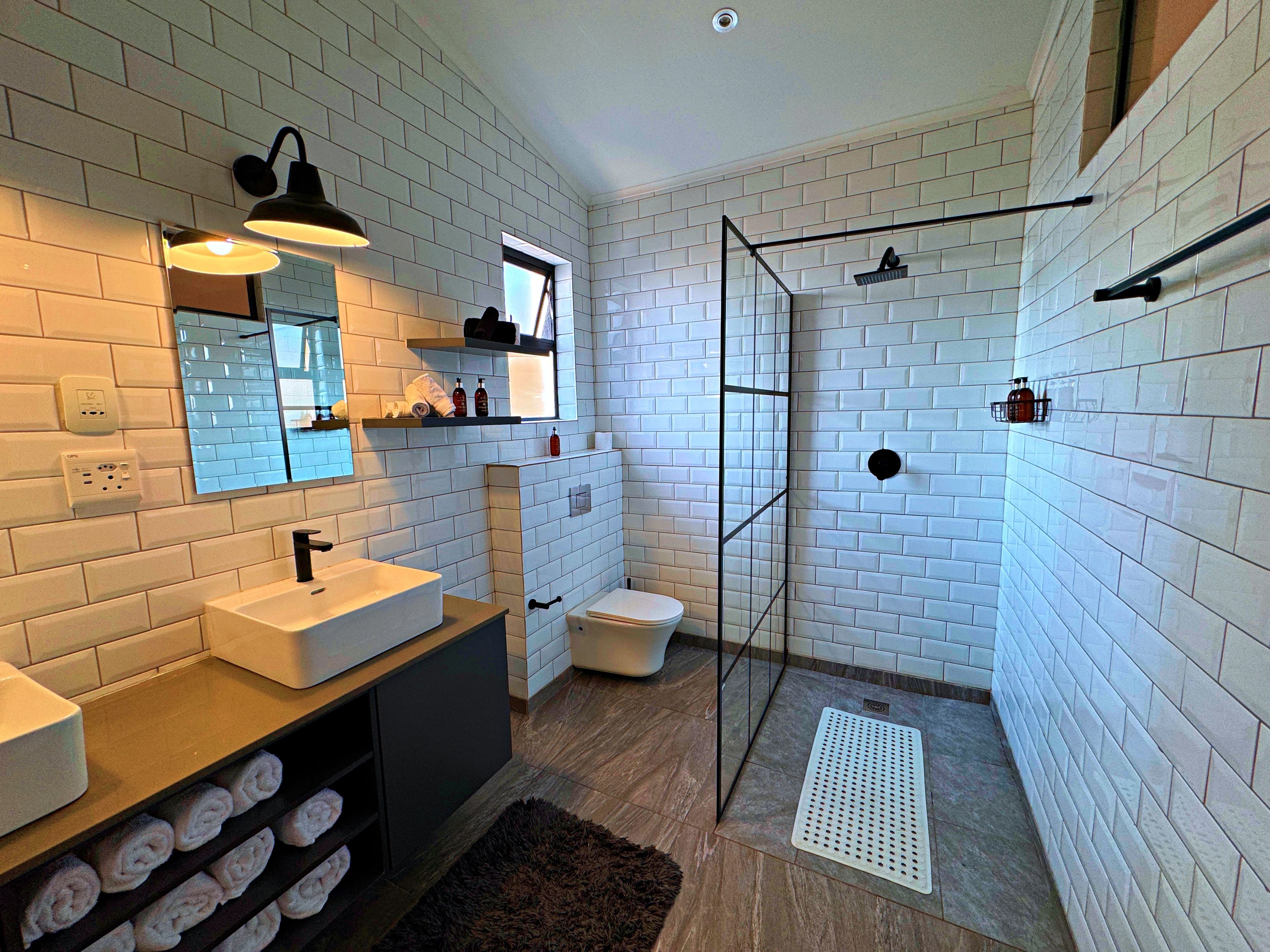 A modern bathroom with white subway tiles, a glass shower enclosure, a white sink, and a mirror with a light fixture.