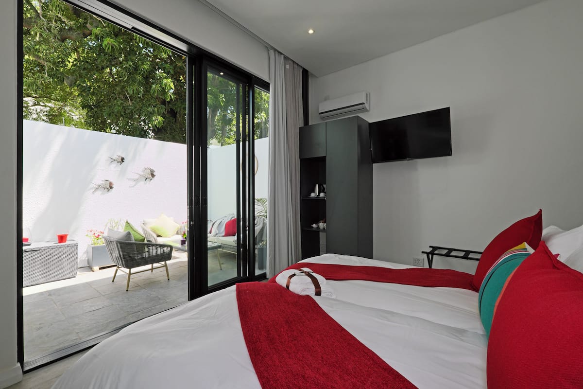 A modern hotel room with a large bed, a TV mounted on the wall, and a sliding glass door leading to an outdoor seating area.