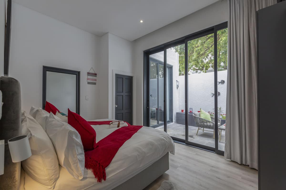 A modern bedroom with a large bed, a sliding glass door to an outdoor area, and a view of the outdoors.