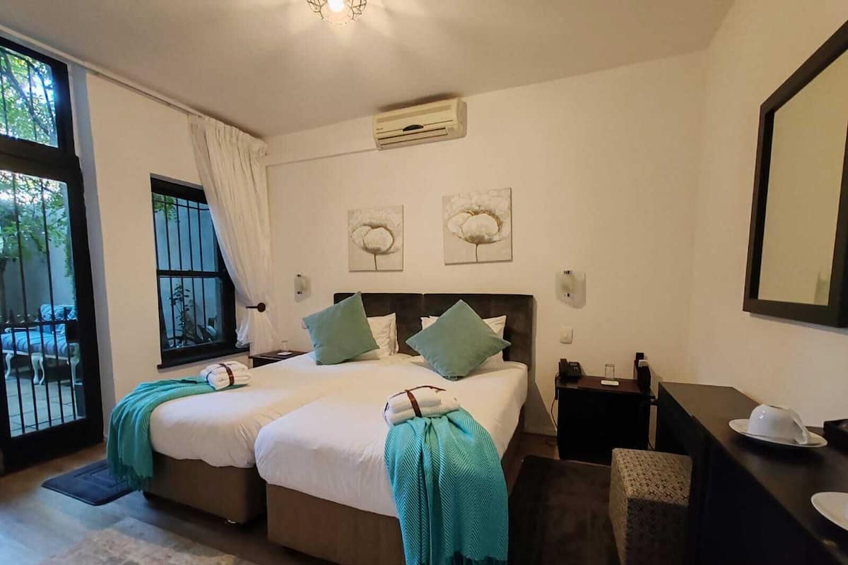 A double bed with a headboard, a bedside table, a desk with a chair, and a window with curtains.