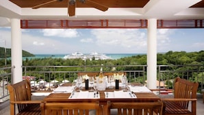 Un coin repas avec une table dressée pour quatre personnes, offrant une vue panoramique sur l’océan et la végétation environnante.