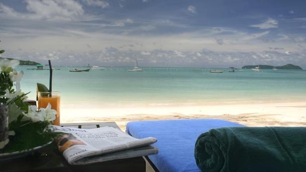 Une vue sur la plage, avec une table décorée de fleurs, un verre de jus d’orange et une serviette.