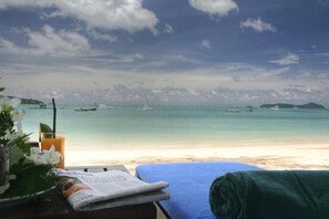 A beach view with a table set with flowers, a glass of orange juice, and a towel.