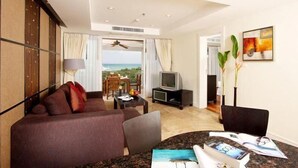 Une chambre d’hôtel avec un canapé, une télévision, une table à manger avec des livres, et une vue sur l’océan.