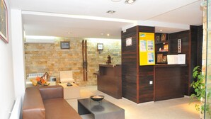 A modern lobby with a stone wall, a wooden reception desk, a sofa, and a small table with a bowl. - Hotel Elitsa (Bansko)