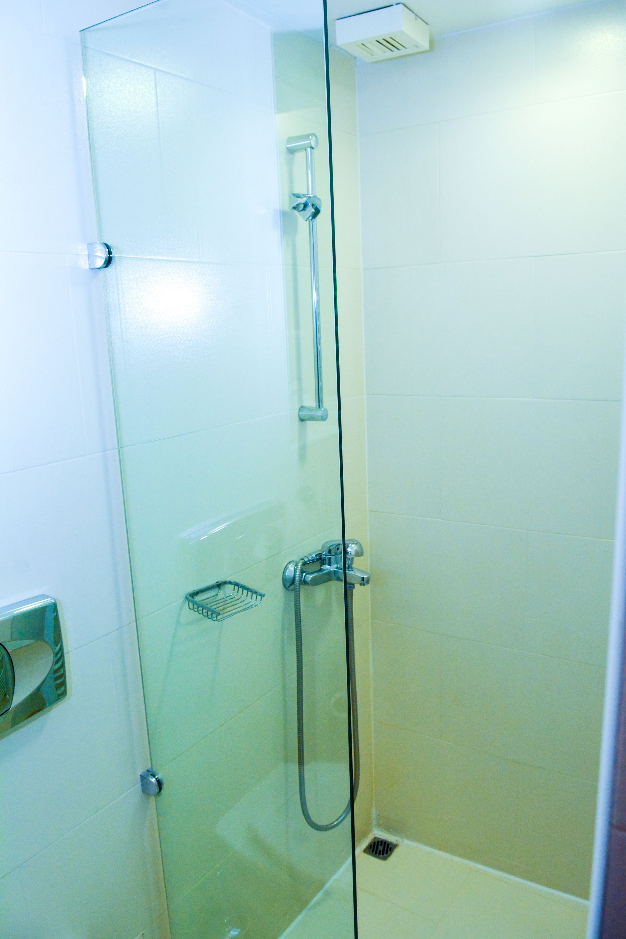 A glass-enclosed shower stall with a handheld showerhead, a towel dispenser, and a small shelf.