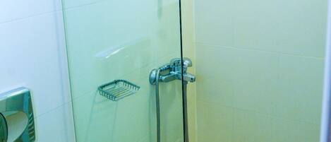 A glass-enclosed shower stall with a handheld showerhead, a towel dispenser, and a small shelf.