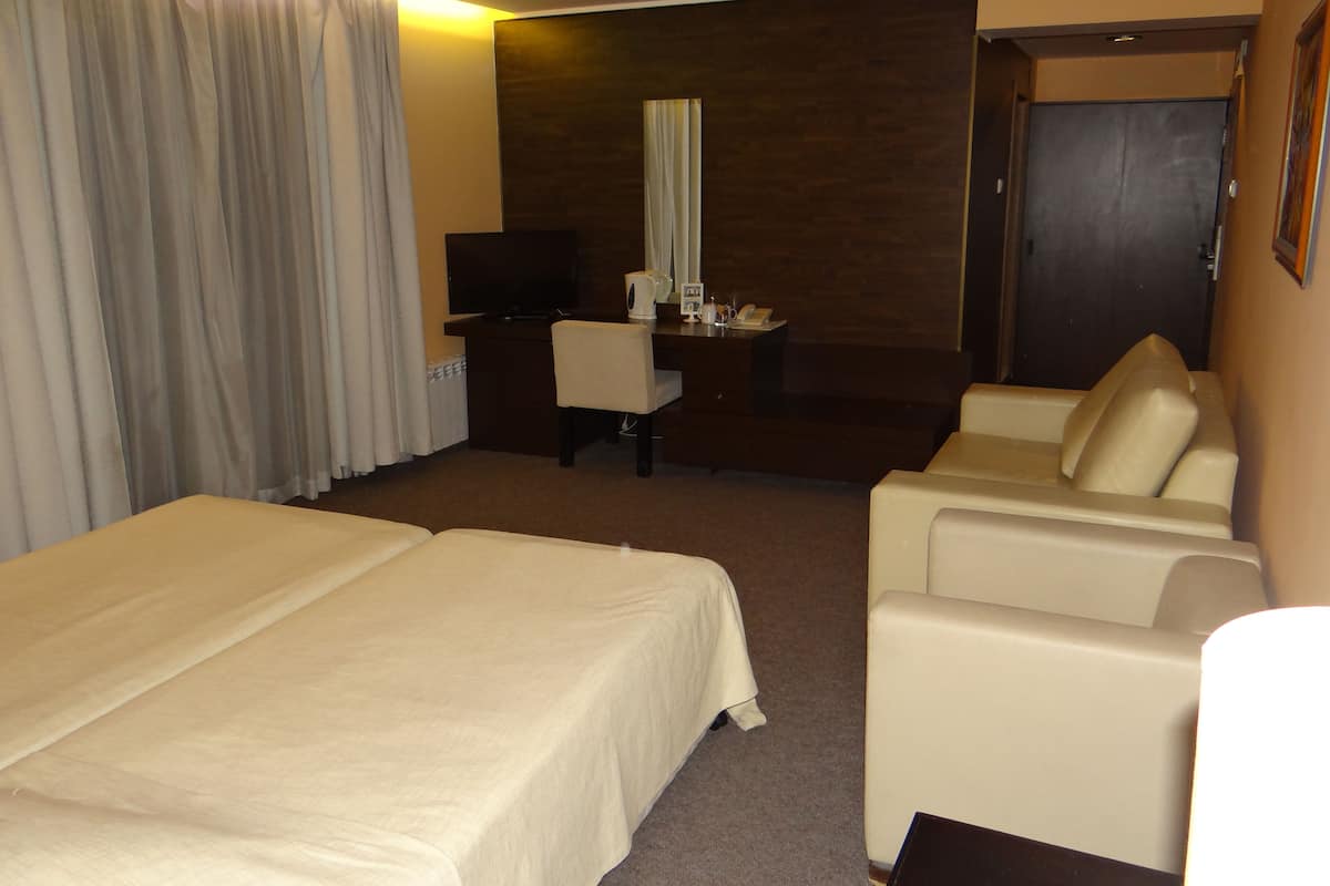 A hotel room with two beds, a desk with a chair, a television, and a seating area with a sofa.