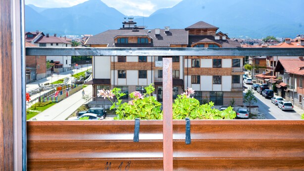 A balcony with wooden railings overlooking a street with parked cars and buildings.