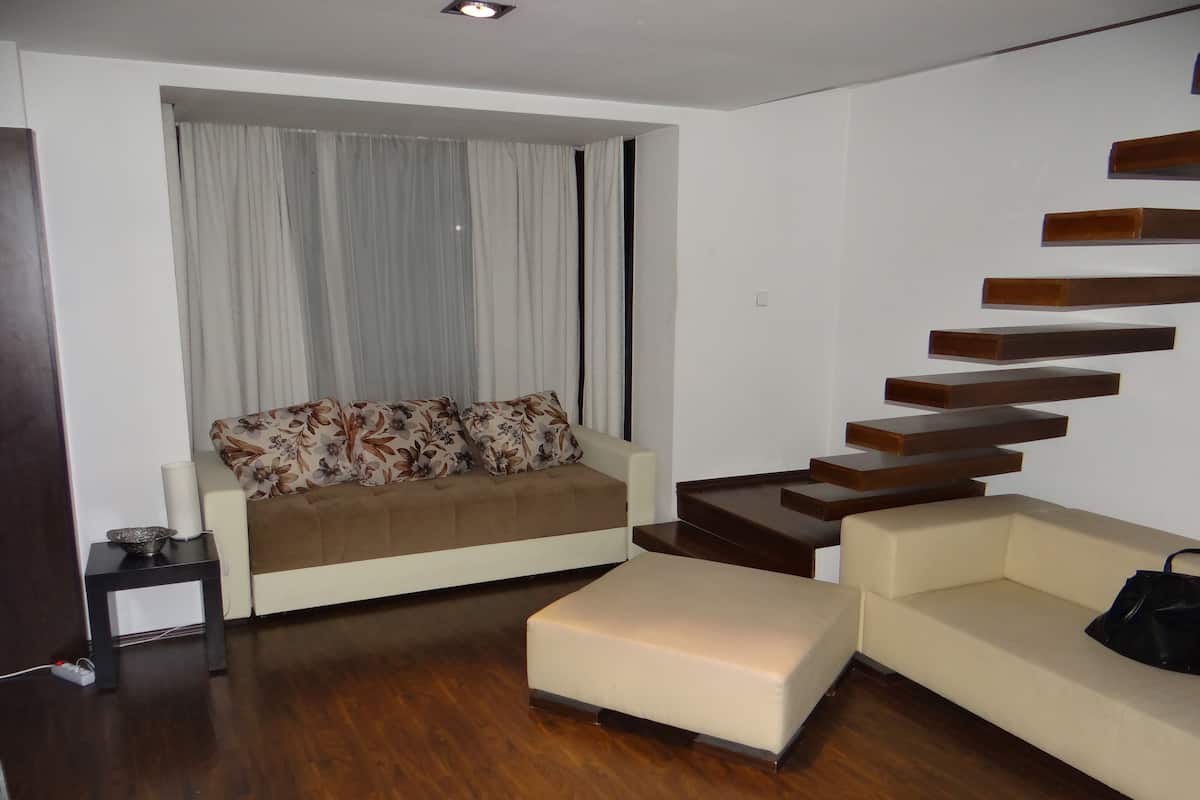 A modern living room with a sofa, a coffee table, a staircase, and a window with curtains.