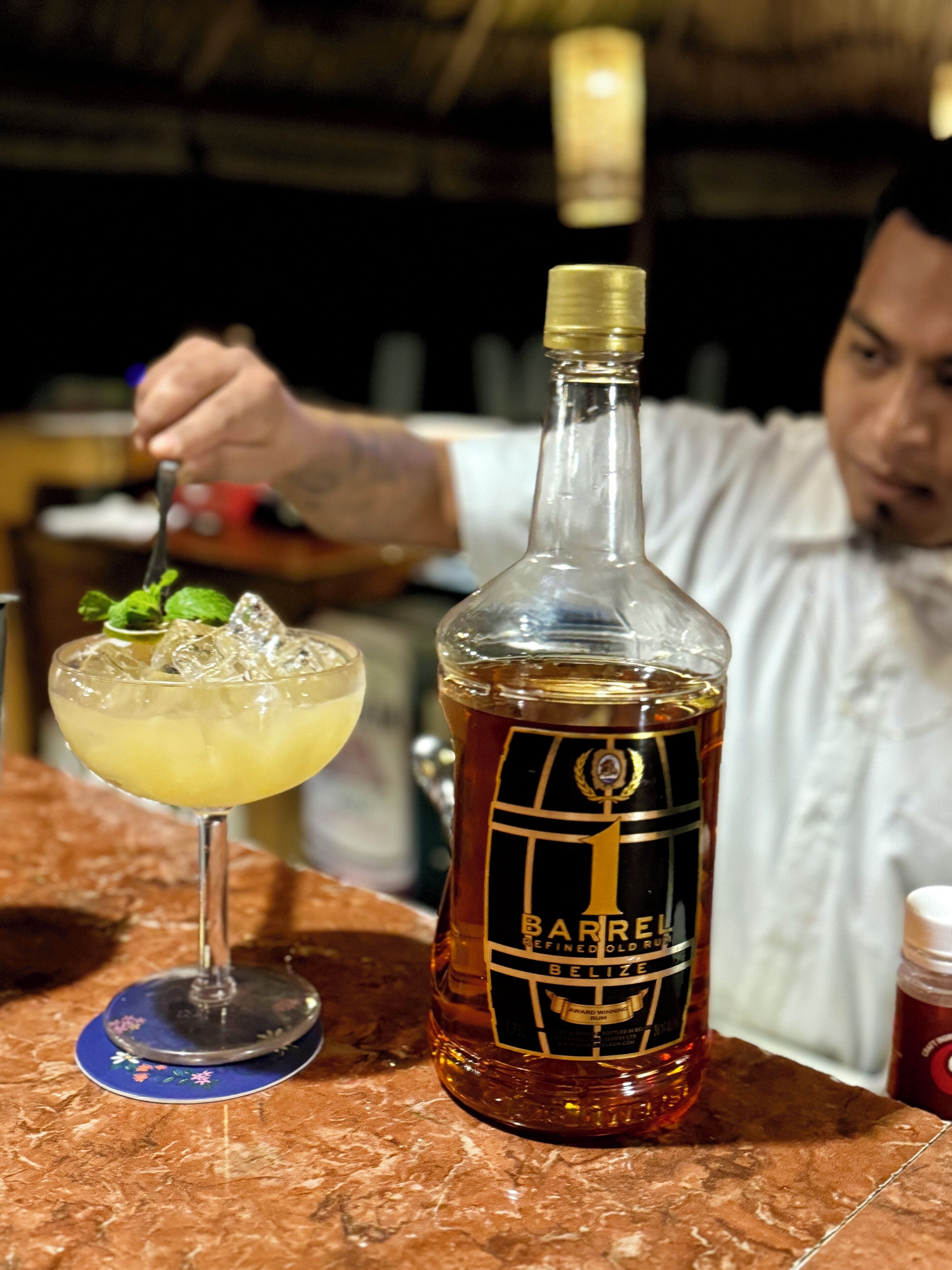 A bottle of Barrel defined old rum and a cocktail with ice on a marble countertop.