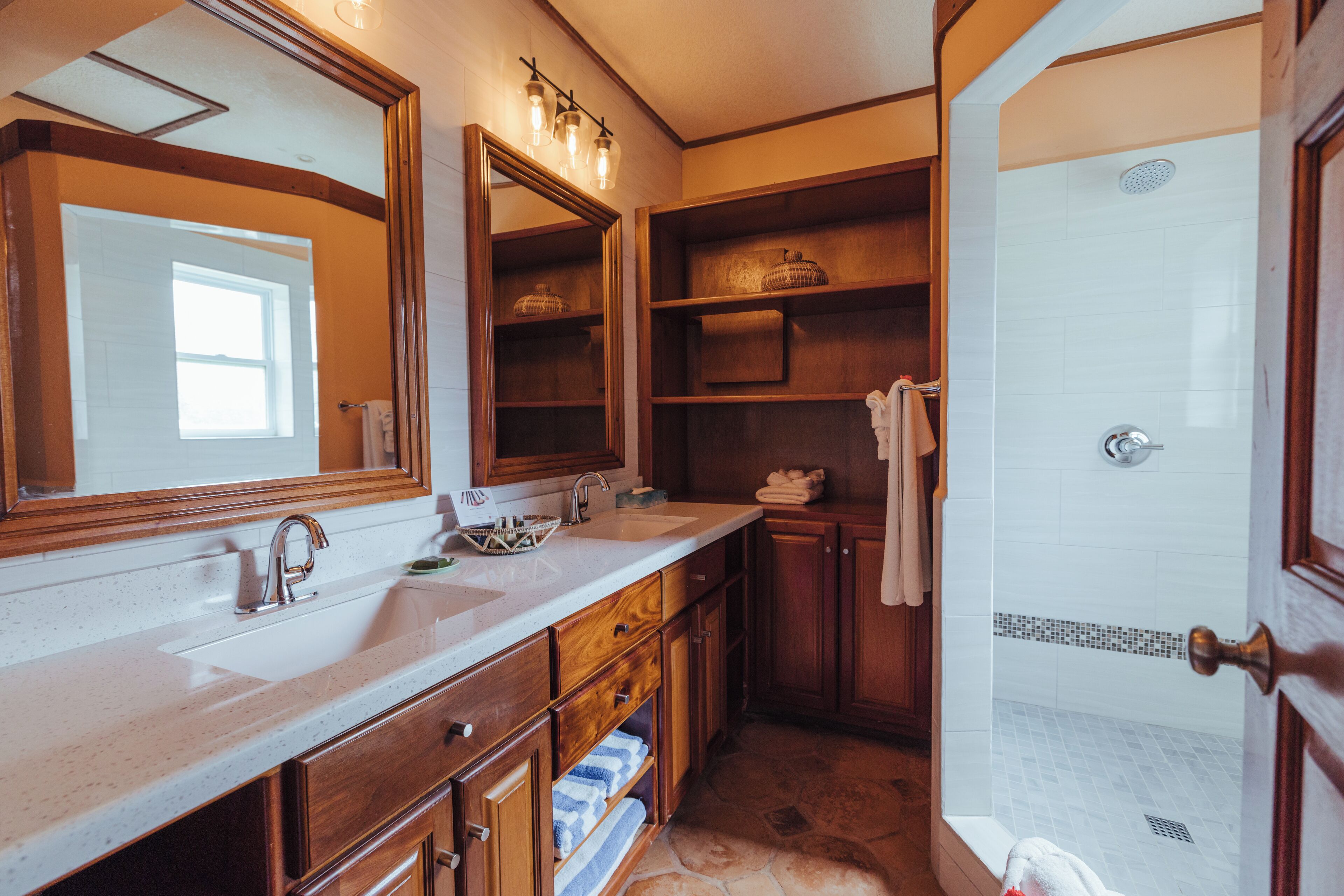 A bathroom with a large mirror, wooden shelves, a sink, and a shower area.