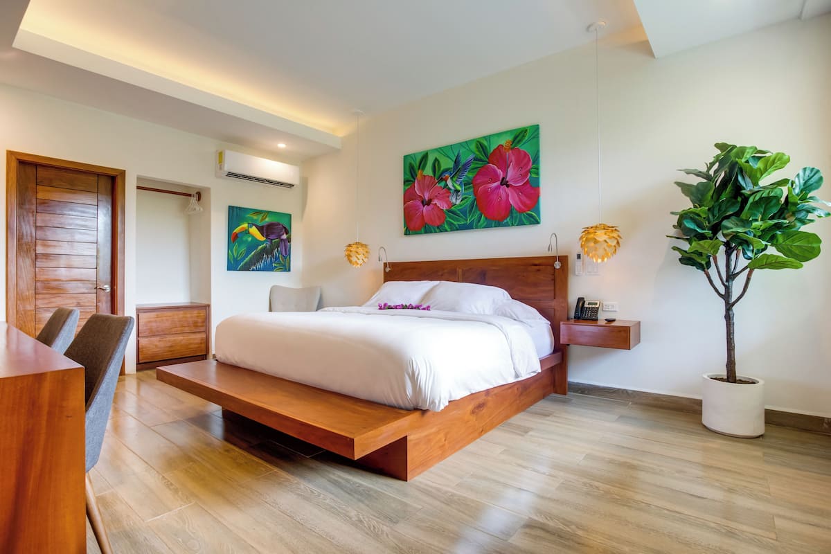 A modern bedroom with a wooden bed, a desk, and a potted plant.