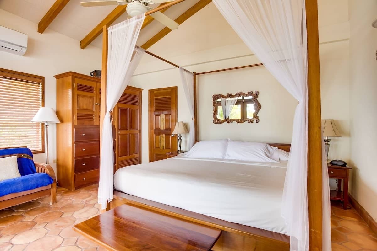 A bedroom with a four-poster bed, wooden wardrobe, and a blue chair.