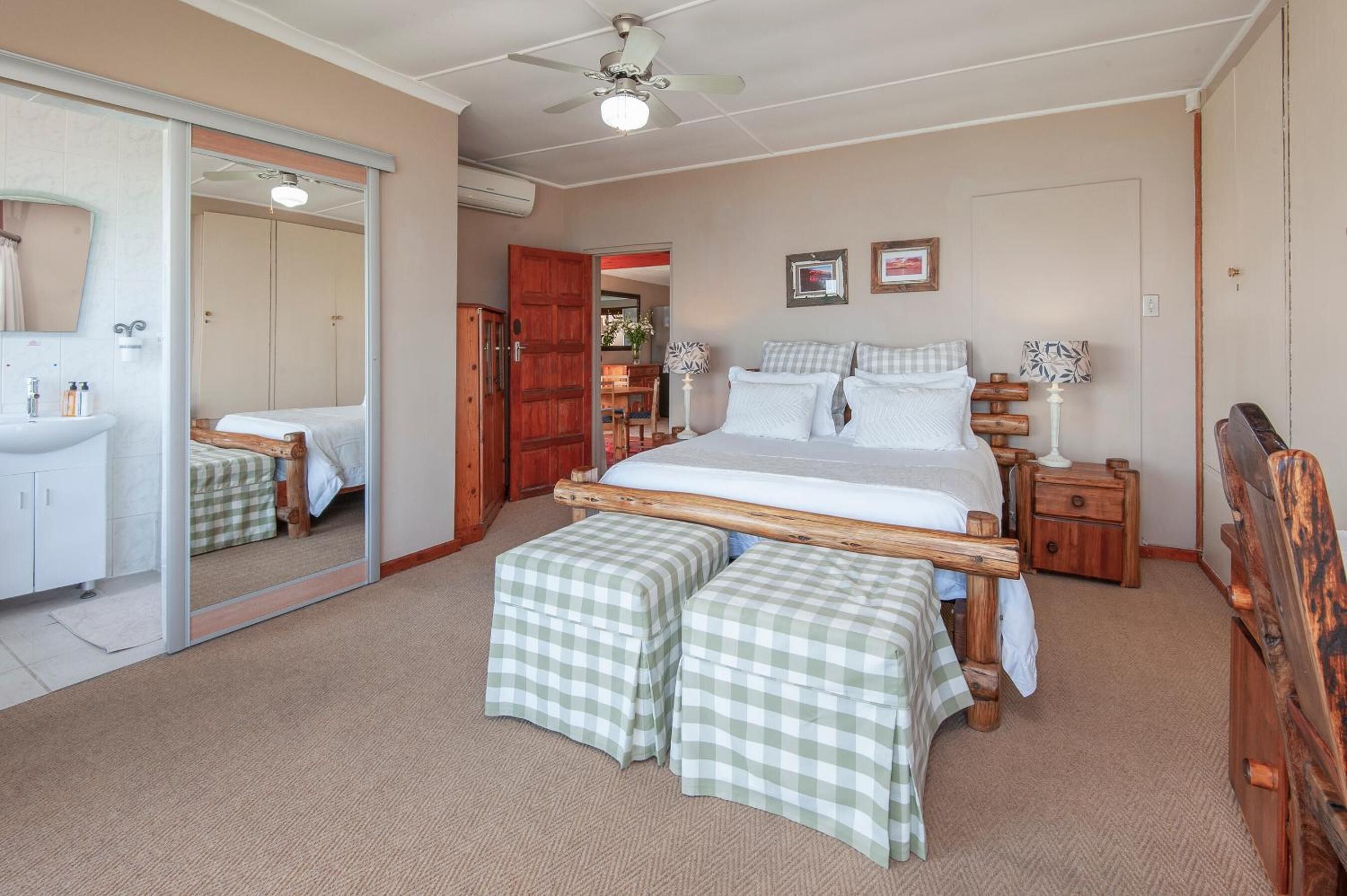 A bedroom with a wooden bed, two bedside tables, a mirror, a wardrobe, and a bathroom with a sink and mirror.