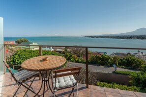 Un balcón con mesa y sillas de madera, con vista al mar y una montaña al fondo.