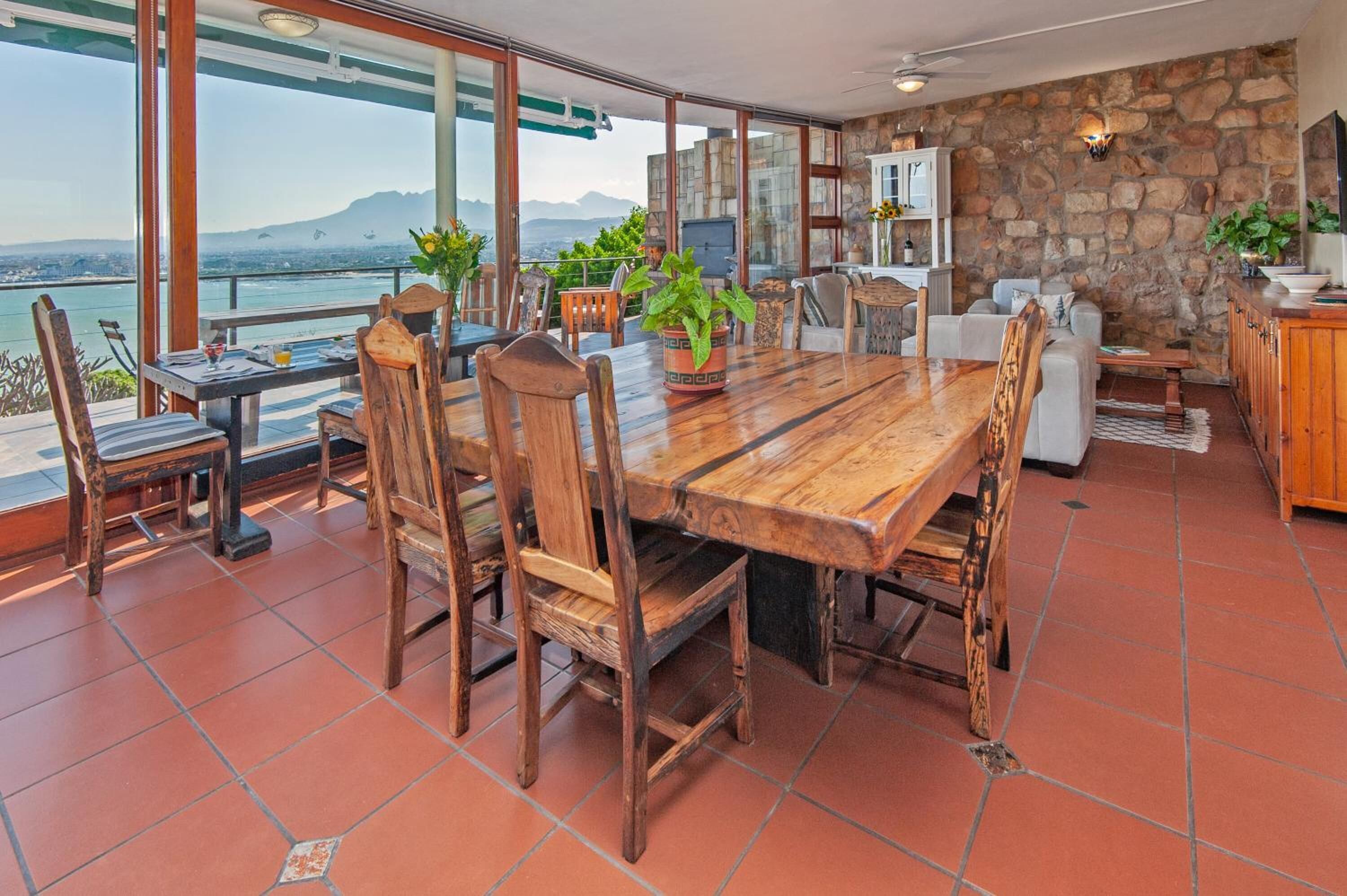 Un'ampia veranda con tavolo e sedie in legno, un muro in pietra e vista sul mare.