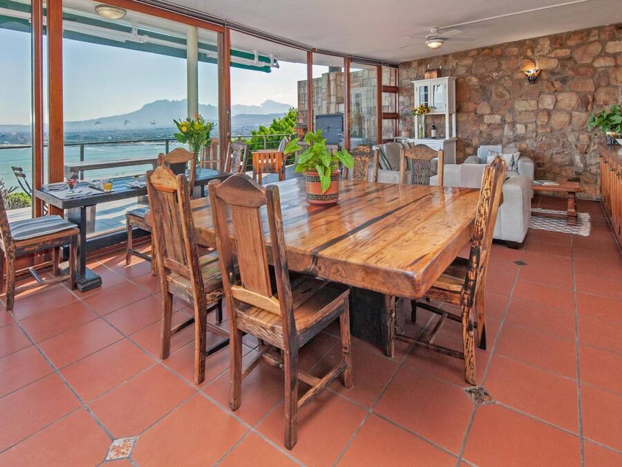 Un'ampia veranda con tavolo e sedie in legno, un muro in pietra e vista sul mare.