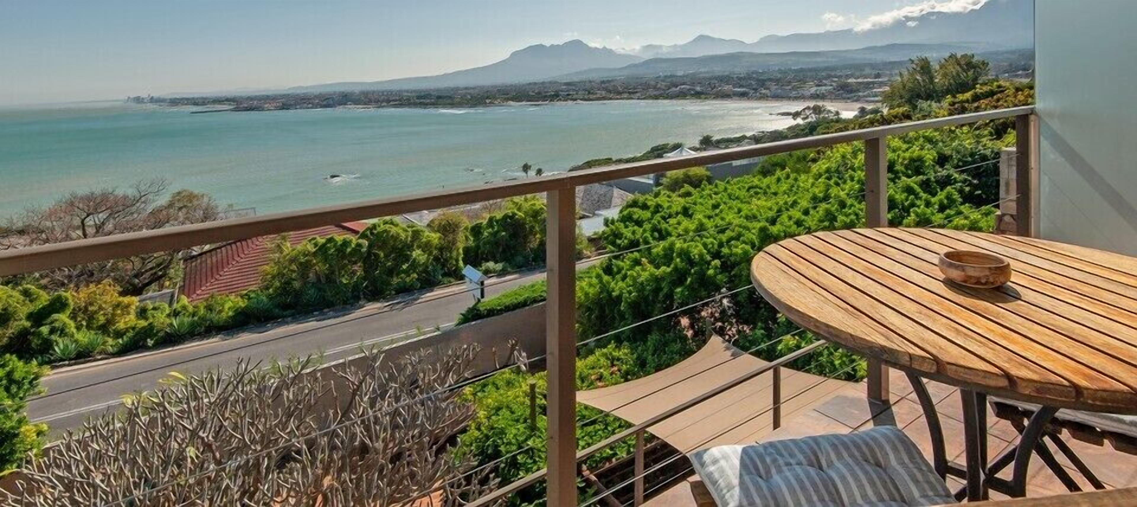A balcony with a wooden table and a view of the sea and mountains.