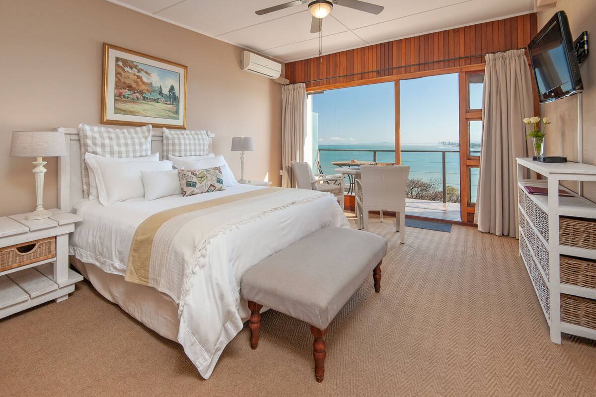 Ein Hotelzimmer mit einem großen Bett, einem Schreibtisch, einem Stuhl, einem Fernseher und Blick aufs Meer.
