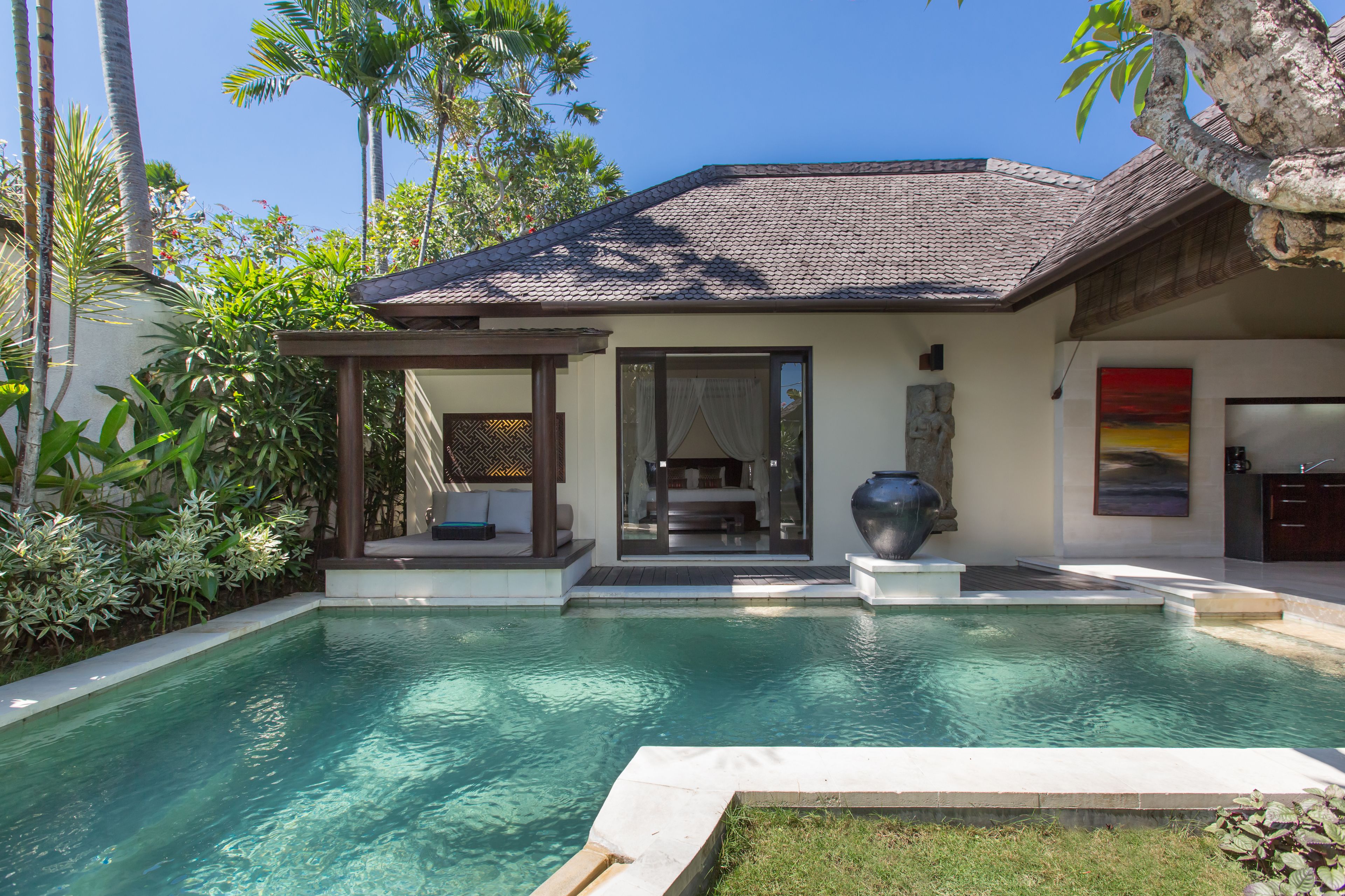 Ein modernes Haus mit Swimmingpool, überdachter Terrasse und einem großen Steinpflanzgefäß.