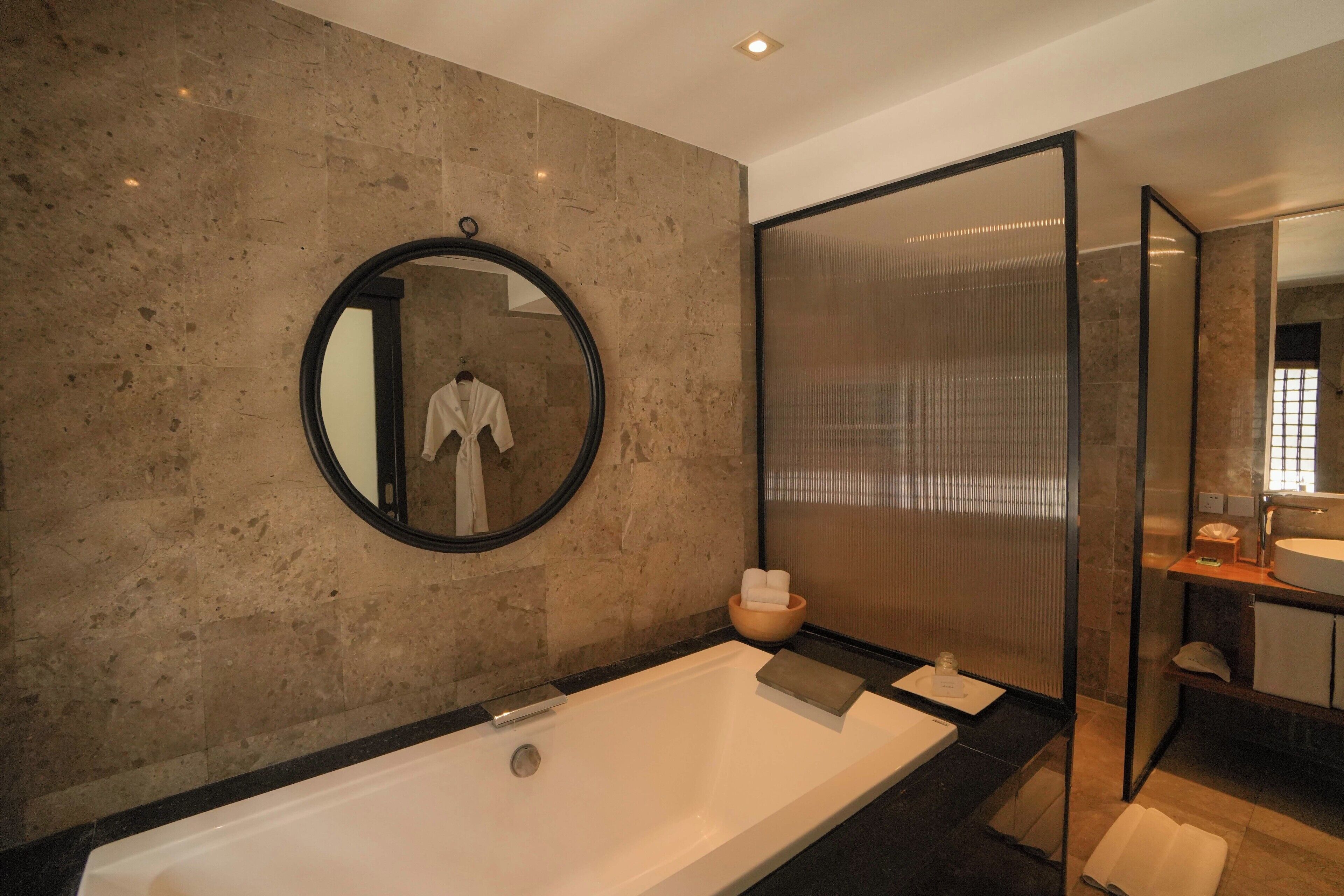 A modern bathroom with a large bathtub, a round mirror, and a glass partition.