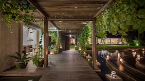 Um caminho de madeira leva a uma área de piscina com plantas pendentes e lanternas.