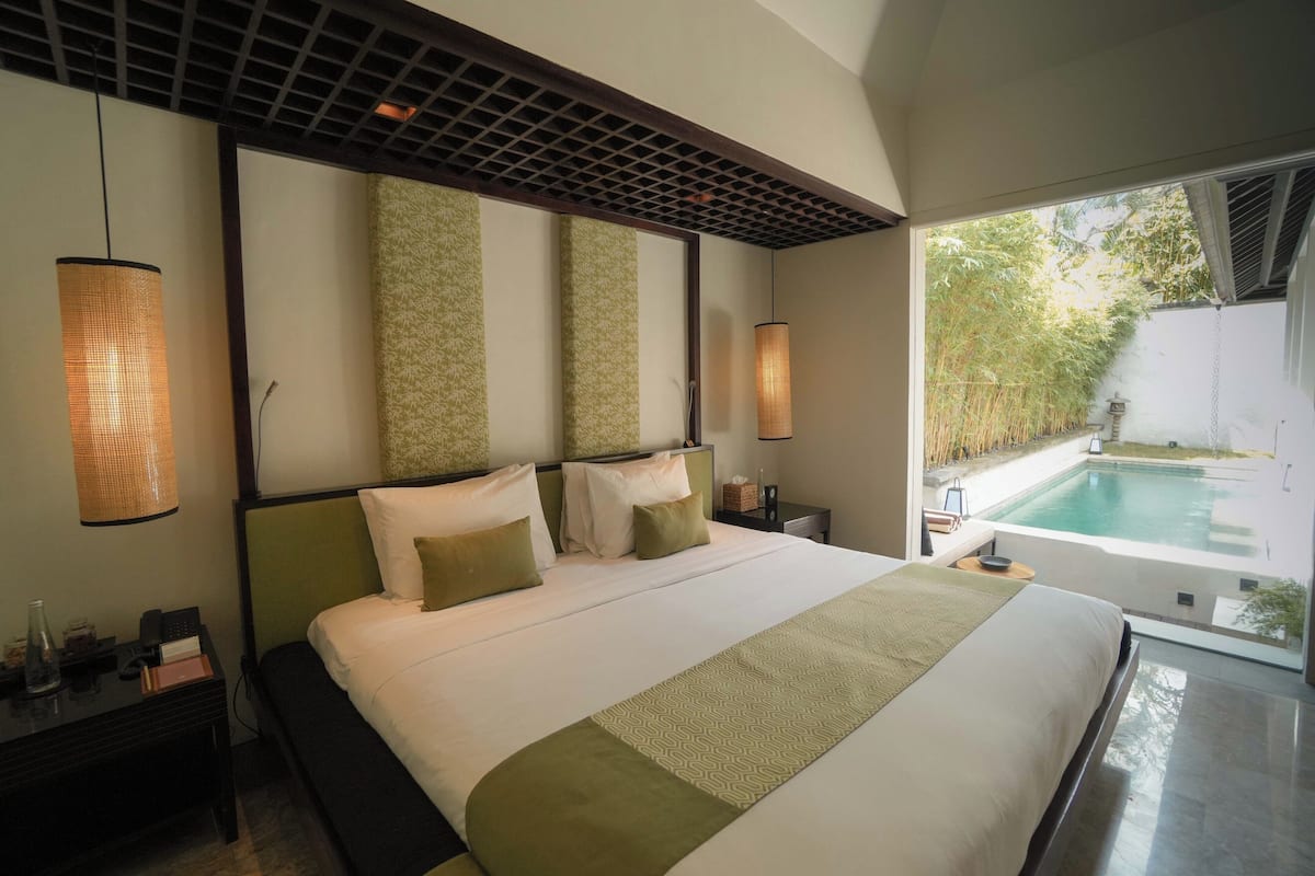 Een moderne hotelkamer met een groot bed, uitzicht op een zwembad en een bamboomschutting buiten.