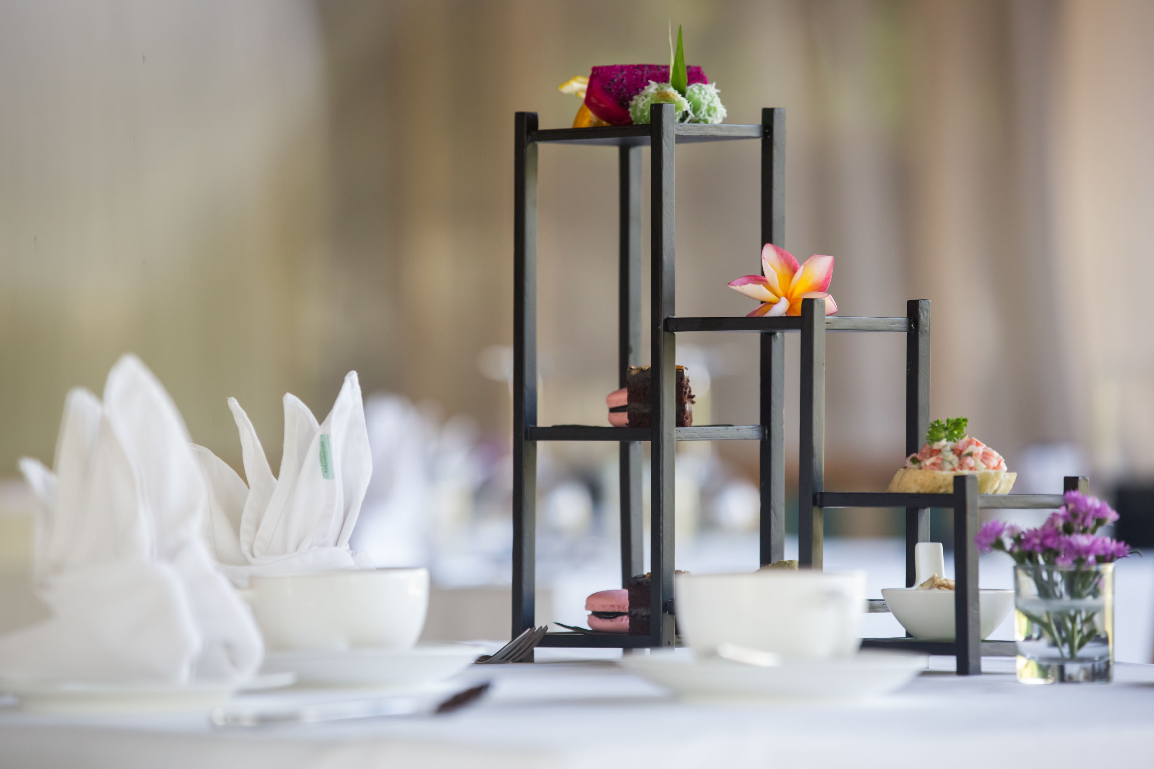 Una mesa con un soporte negro escalonado que sostiene varios objetos, incluyendo un tazón, un florero con flores y una pequeña fuente.