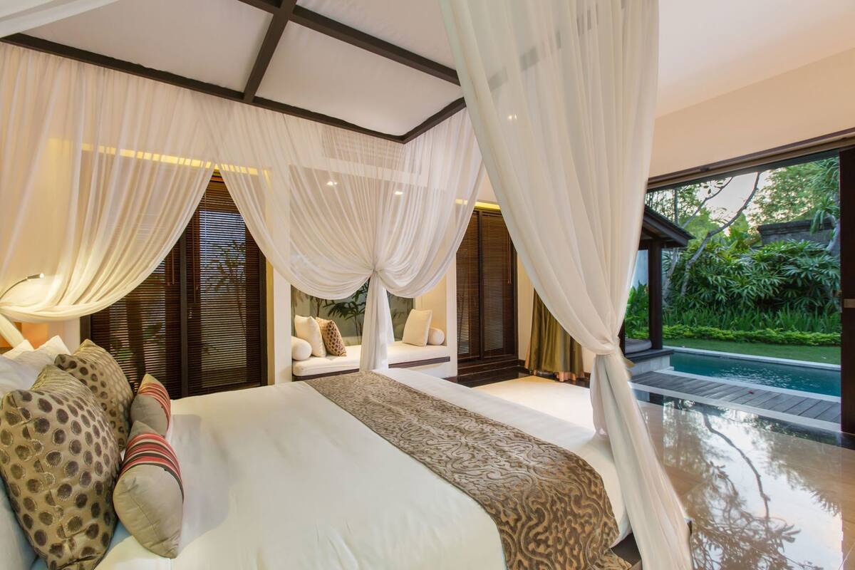 Een slaapkamer met een groot bed, uitzicht op een zwembad en een balkon.