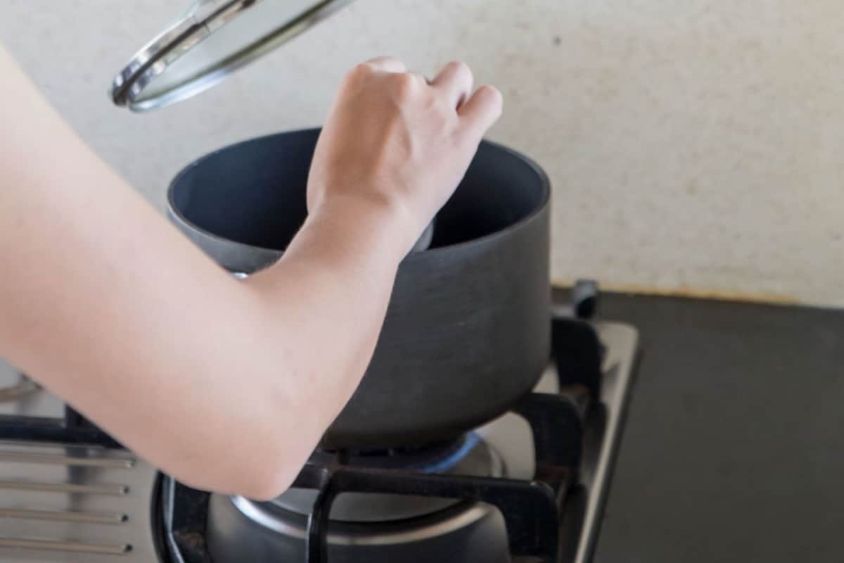 Une personne soulève le couvercle d’une casserole posée sur une cuisinière.