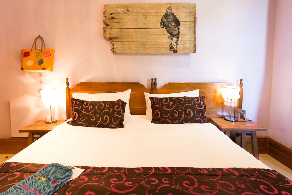 Habitació d'hotel amb un llit gran, dues taules de nit, un panell de fusta al capçal, una obra penjada a la paret i una bossa penjant.