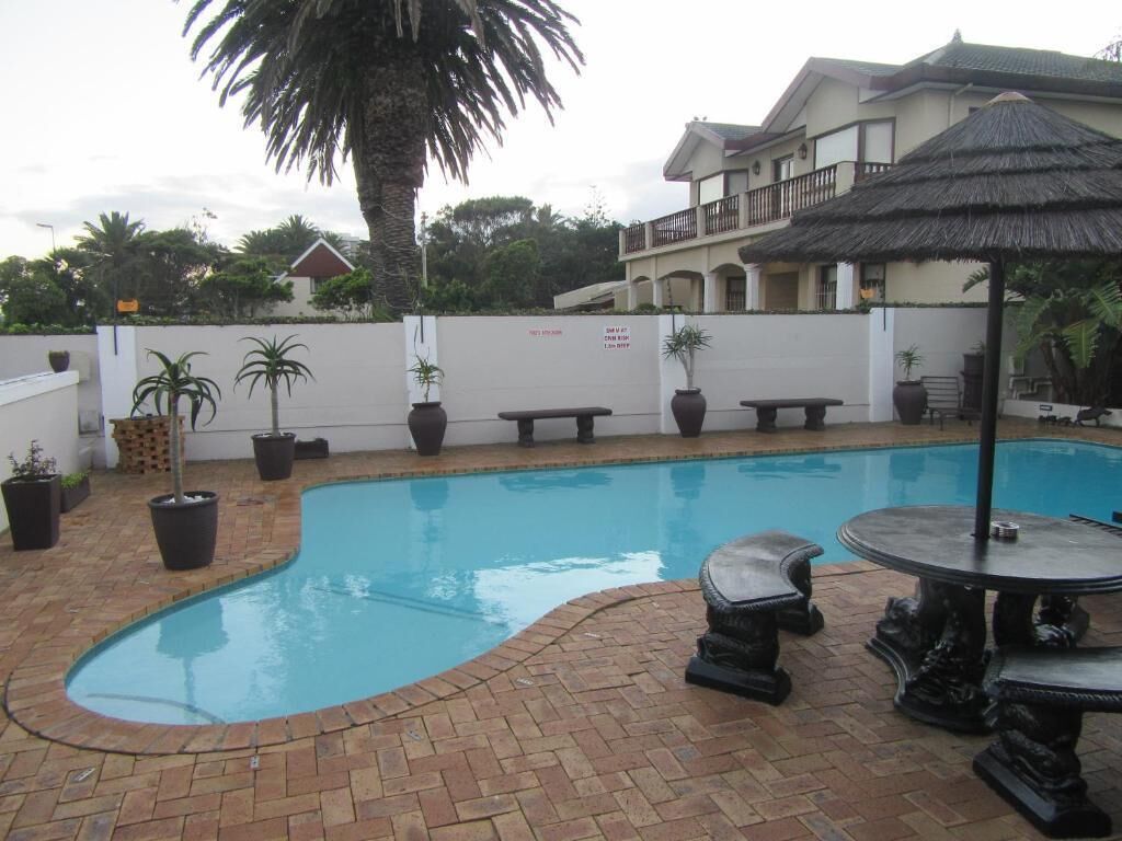 A swimming pool with a brick border, surrounded by potted plants and outdoor furniture.