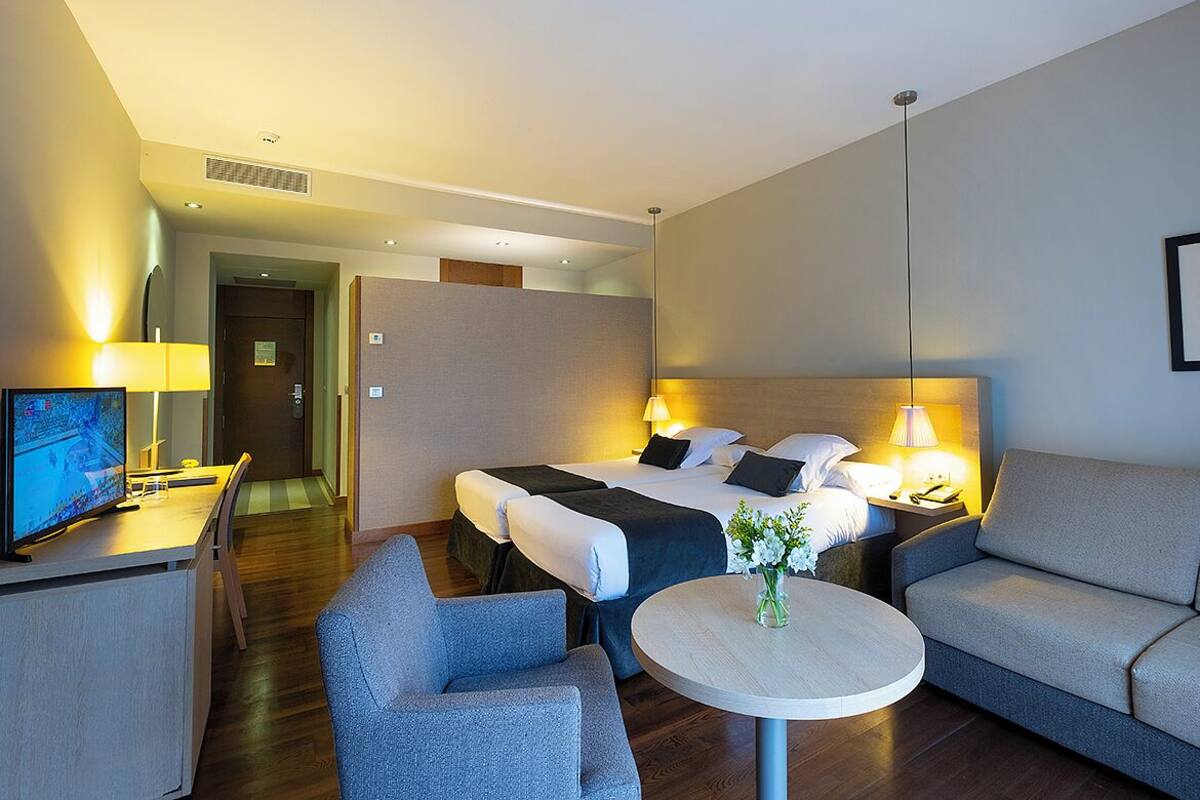Hotelkamer met een bed, een bank, een kleine tafel met een vaas, een televisie en een bureau met een lamp.