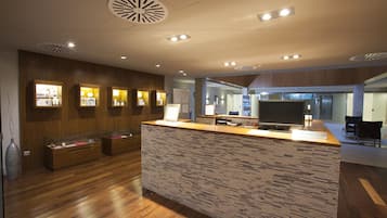 A modern reception area with a wooden reception desk, a large flat-screen TV, and a patterned wall.